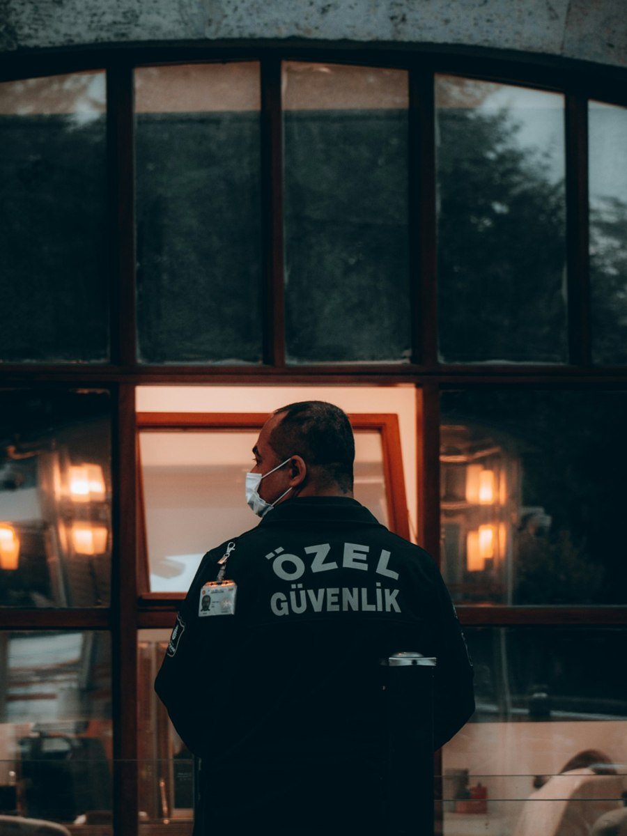 ÖZEL GÜVENLİK yazılı ceketiyle bina girişinde nöbet tutan özel güvenlik görevlisi (temsili görsel)